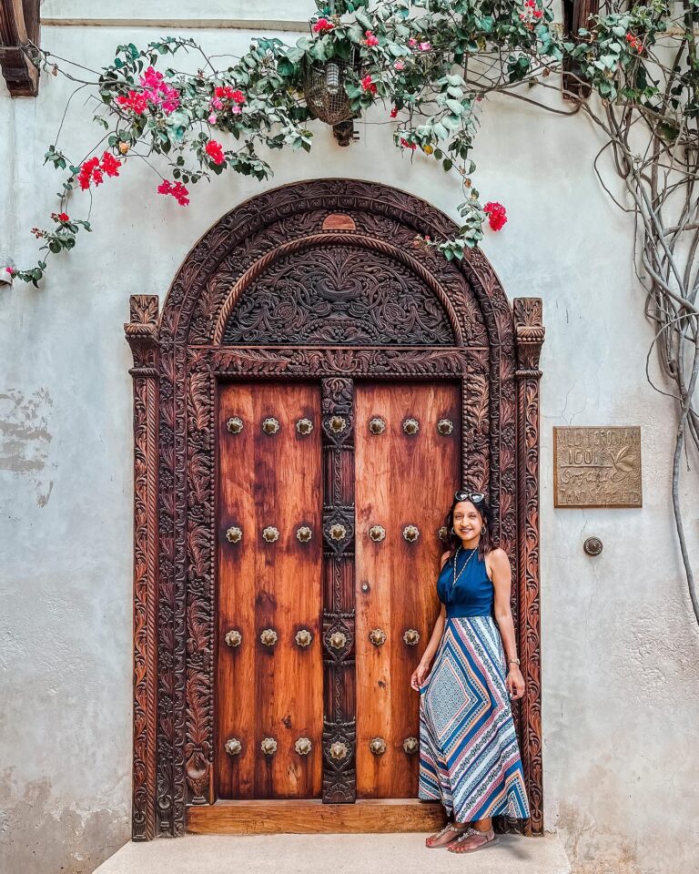 A carved wooden door on a Stone Town street, framed by bougainvillea